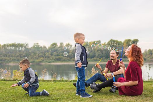 People and nature concept - Mother, father and their child playing with colorful soap bubbles.