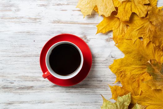Flat lay autumn composition with cup of black tea and yellow autumn leaves. Time of tea break concept. Hot beverage lies on vintage wooden desk with bright foliage. Still life of morning tea ceremony.