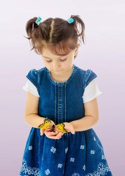 Adorable little girl with short pigtails on her head, holding a large butterfly, close-up.Not a purple gradient background.