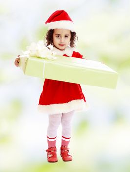 Cute little girl in a coat and hat of Santa Claus, holding a big green box , tied with a bow.white-green blurred abstract background with snowflakes.