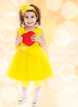 Adorable little girl in bright yellow elegant dress. Close to her heart.Winter brown abstract background with white snowflakes.