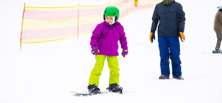 Snowboard Winter Sport. little girl learning to snowboard, wearing warm winter clothes. Winter background.