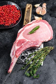 Raw tomahawk pork chop meat steak on a meat cleaver. Black background. Top view.