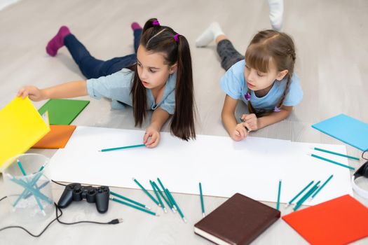 Cute children are painting and smiling while lying on the floor at home