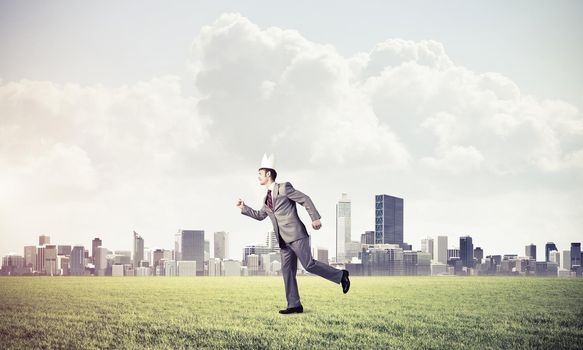 Young handsome businessman wearing white paper crown running in a hurry