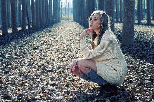 Beautiful blonde girl, dressed with a beige dress, standing in a poplar forest