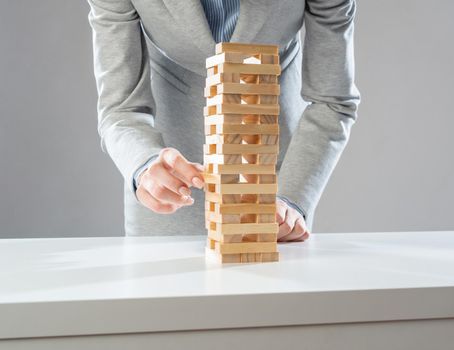 Businesswoman removing wooden block from tower on table. Management of risks concept with wooden box game. Business development and assistance. New challenge and leadership motivation.