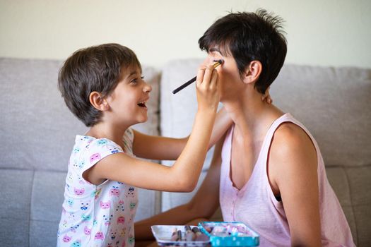 Happy beautiful mother and her little cute daughter doing make up for each other. Mum spending free time with her daughter.