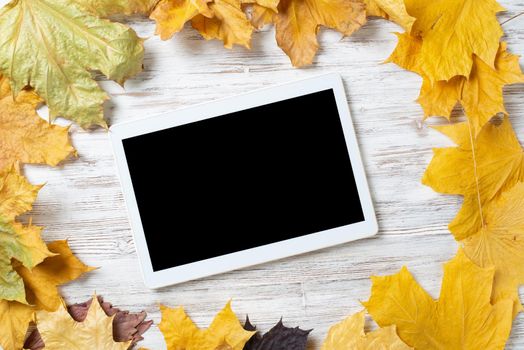 Tablet computer with blank screen lies on vintage wooden desk with bright foliage. Flat lay composition with autumn leaves on white wooden surface. Internet communication and digital technology