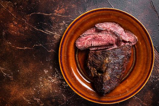 Roasted hanger or Onglet sliced beef meat steak on a rustic plate with cleaver. Dark wooden background. Top View. Copy space.