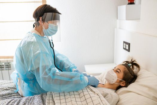 Doctor protected by personal protective equipment examining a little girl with a stethoscope at home.