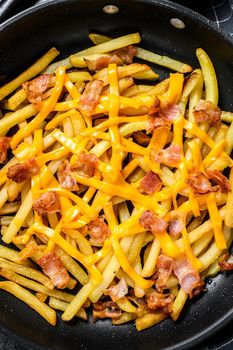 Golden French fries fried with cheddar cheese and bacon in a pan. Black background. Top view.
