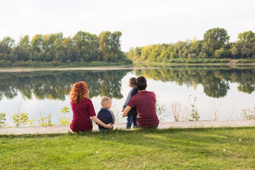 Childhood and nature concept - Family with little sons sitting on the green grass.