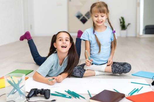 family, leisure and childhood concept - happy sisters lying on floor and drawing and doing homework at home