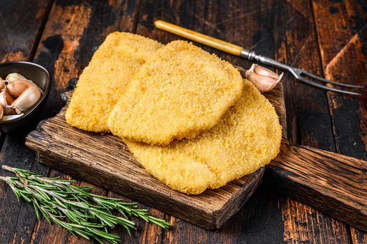 Raw chicken cordon bleu meat cutlets with bread crumbs on a wooden board. Dark wooden background. Top view.