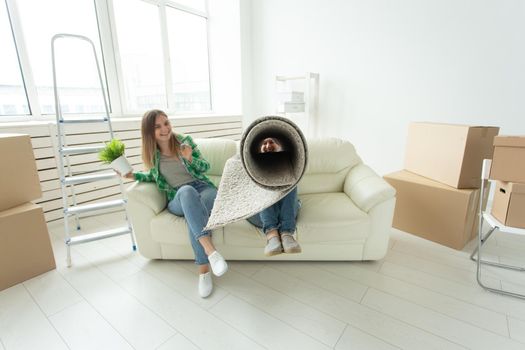 Cheerful joyful young couple charming girl and handsome man holding a box with things and a pot with a plant while moving to a new apartment. Housewarming and mortgage concept