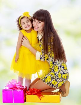 Slender young mother in a short elegant dress and her cute little daughter , embracing, surrounded by Christmas gifts.white-green blurred abstract background with snowflakes.