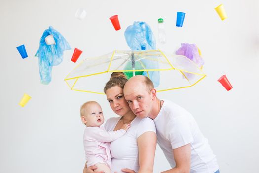 Environmental pollution, plastic recycling problem and waste disposal concept - surprised family under garbage on white background