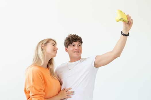 Funny crazy young couple blonde girl and a hipster guy taking a selfie on a vintage yellow film camera posing on a white background. Concept of photography hobby. Advertising space