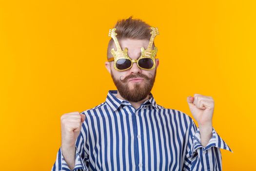 Positive young man with glasses in the form of guitars rejoices having lifted his hands up against a yellow background. The concept of celebration and parties. Advertising space