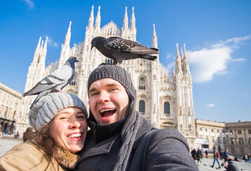 Winter travel and vacations concept - Happy tourists taking a self portrait with funny pigeons in front of Duomo cathedral in Milan.