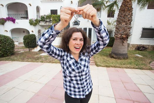 Real estate and property concept - Happy young woman in front of new home with new house keys.