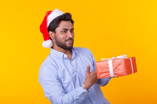 Positive young man Santa Claus with gifts and Christmas tree posing on a yellow background. Christmas and New Year holidays concept. Advertising space