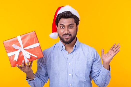 Positive young man Santa Claus with gifts and Christmas tree posing on a yellow background. Christmas and New Year holidays concept. Advertising space