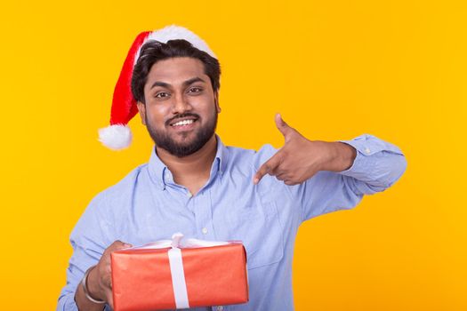 Positive young man Santa Claus with gifts and Christmas tree posing on a yellow background. Christmas and New Year holidays concept. Advertising space