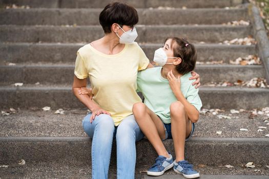 Middle-aged mother and daughter sit on the street wearing masks because of the Covid-19 pandemic