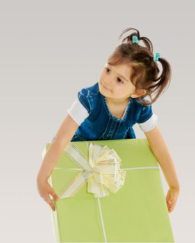 Pretty little girl in blue dress with short sleeves , holding a gift,which lies in a large green box. Close-up.On a gray background.