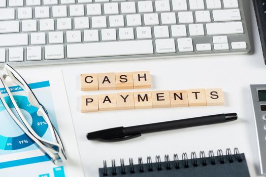 Cash payments concept with letters on wooden cubes. Still life of office workplace with supplies. Flat lay white surface with computer keyboard and notepad. Financial management and accounting.