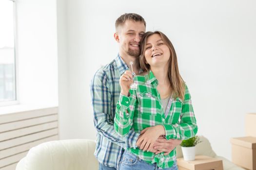 Charming young woman and her husband holding in hands the keys to their new apartment while sitting in her new living room. Housewarming and mortgage in new building concept.