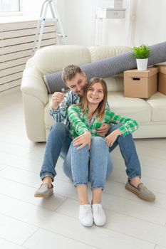 Young positive couple holding keys to a new apartment while standing in their living room. Housewarming and family mortgage concept