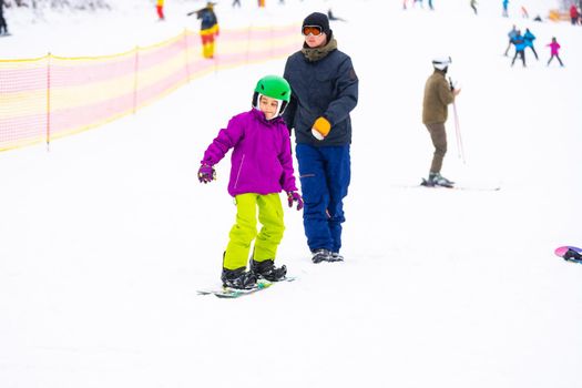 Instructors teach a child on a snow slope to snowboard