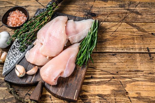 Fresh Raw sliced cut chicken breast fillet steaks on a wooden cutting board with kitchen knife. wooden background. Top view. Copy space.