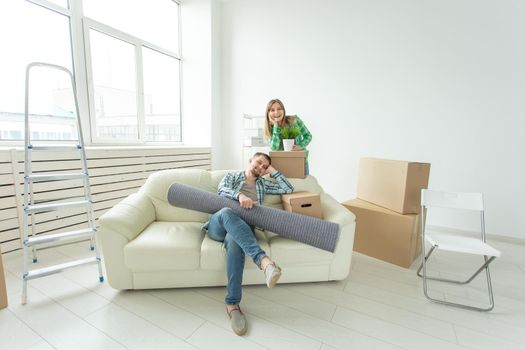 Satisfied cheerful young couple strong man and pretty woman holding their things in their hands sitting in the living room of a new apartment. Housewarming concept