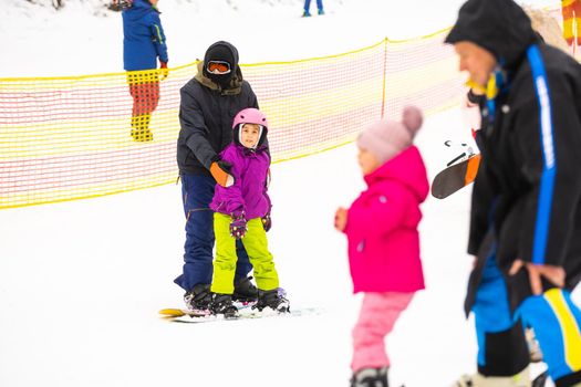 Instructors teach a child on a snow slope to snowboard