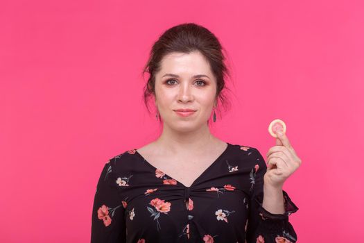 Safe sex, health and contraception concept - woman holding in hands a condom on pink background.