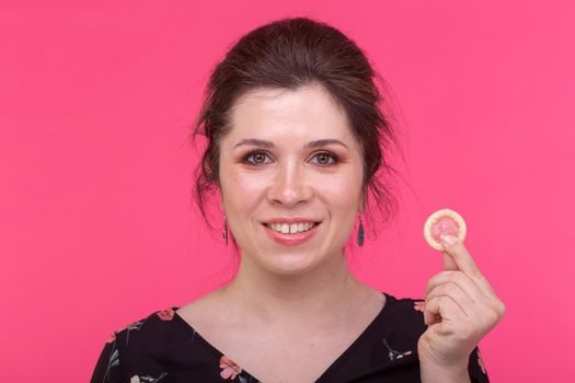 Safe sex, health and contraception concept - woman holding in hands a condom on pink background.