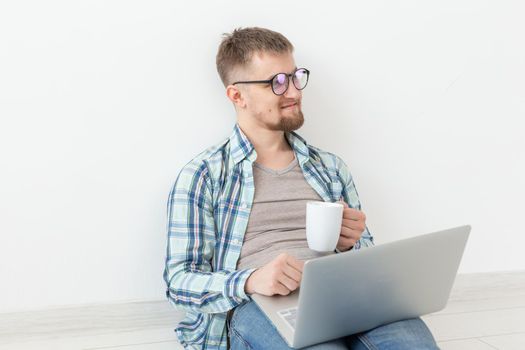 Positive young man in casual clothes and glasses surfing the Internet using Wi-Fi and a laptop in search of rental housing. Housewarming and apartment search concept