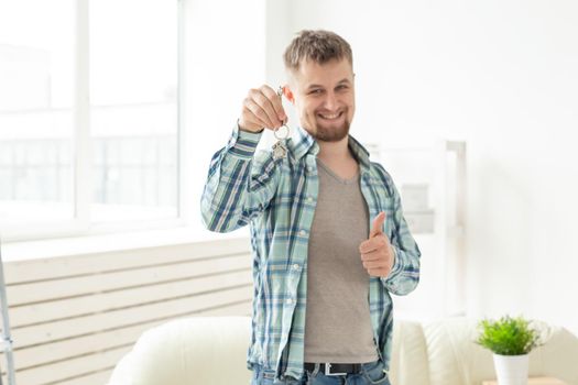 Young handsome guy shows the keys to his new apartment while standing in the living room. Mortgage and home loan concept for a young family