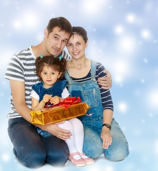 Happy young family with little daughter cuddling together in celebration of Christmas.Blue Christmas festive background with white snowflakes.
