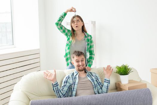 Young positive couple holding keys to a new apartment while standing in their living room. Housewarming and family mortgage concept