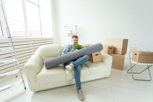 Positive young man sitting on the sofa with his things in the new living room after the move and shows a thumbs up. Concept of housing affordability for young people