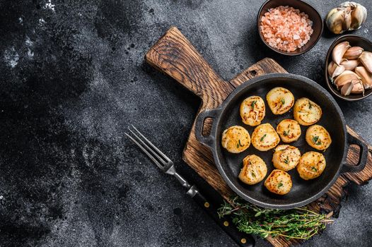 Fried scallops with butter sauce in a pan. Black background. Top view. Copy space.