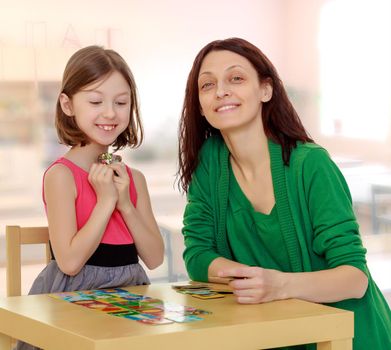 Joyful little girl and her mother at the table laid out cards with pictures.During a lesson in school.