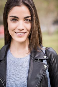 Close-up portrait of young woman smiling in urban background wearing casual clothes. Girl wearing striped sweater and leather jacket