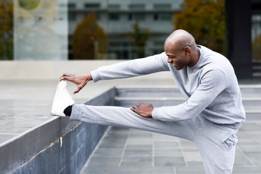 Black man doing stretching before running in urban background. Young male exercising
