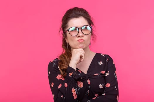 Close-up portrait of pensive serious young charming woman in glasses posing on a pink background. Concept of dreams and ideas. Advertising space